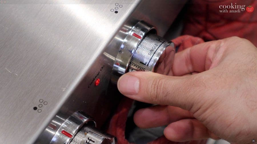 Hand adjusting stovetop burner dial while heating water for double boiler chocolate melting.