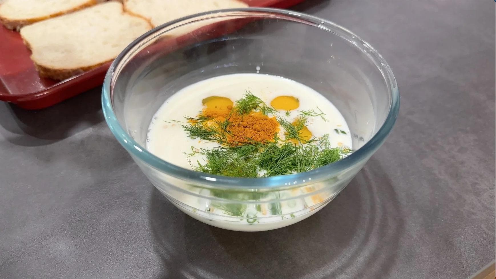 Egg mixture with milk, eggs, turmeric, coriander, and fresh dill in a glass bowl, ready for dipping bread.