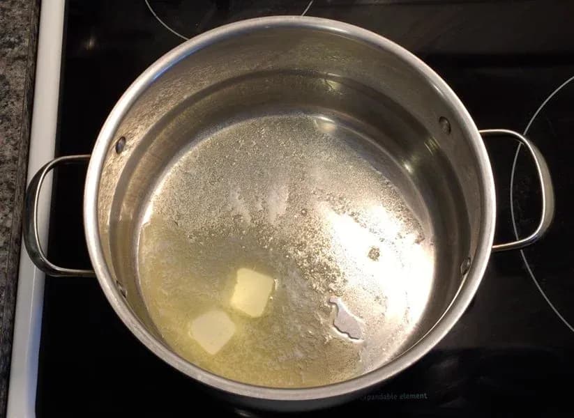 Melted butter with spices in a stainless steel pot on a stovetop for makhani sauce.