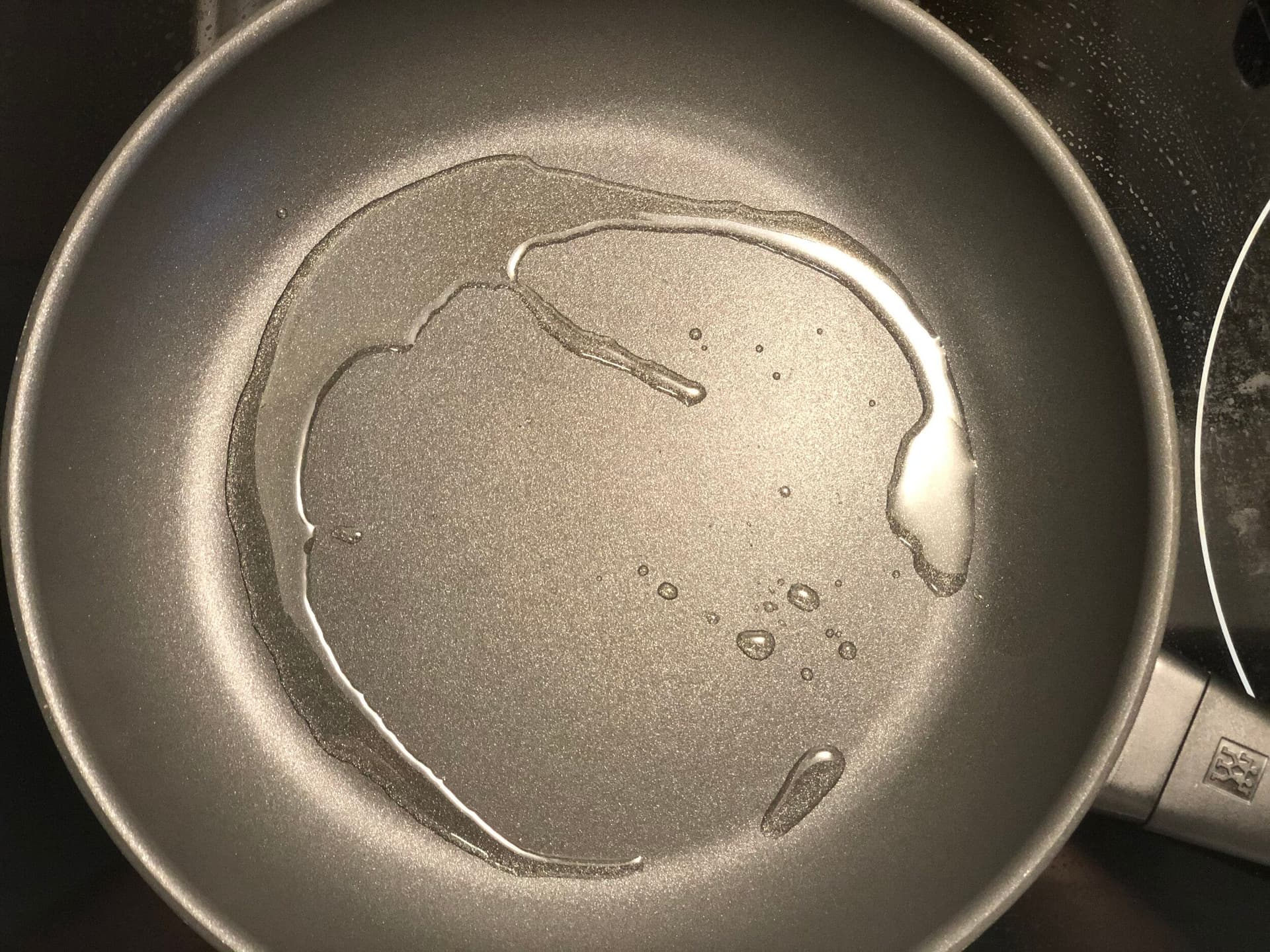 Oil heating in a pan with cumin seeds crackling, shown as small brown specks floating in the hot oil.
