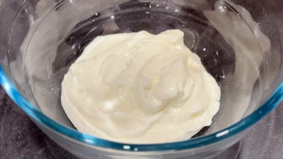Creamy yogurt and dill sauce mixed in a glass bowl for German cucumber salad.