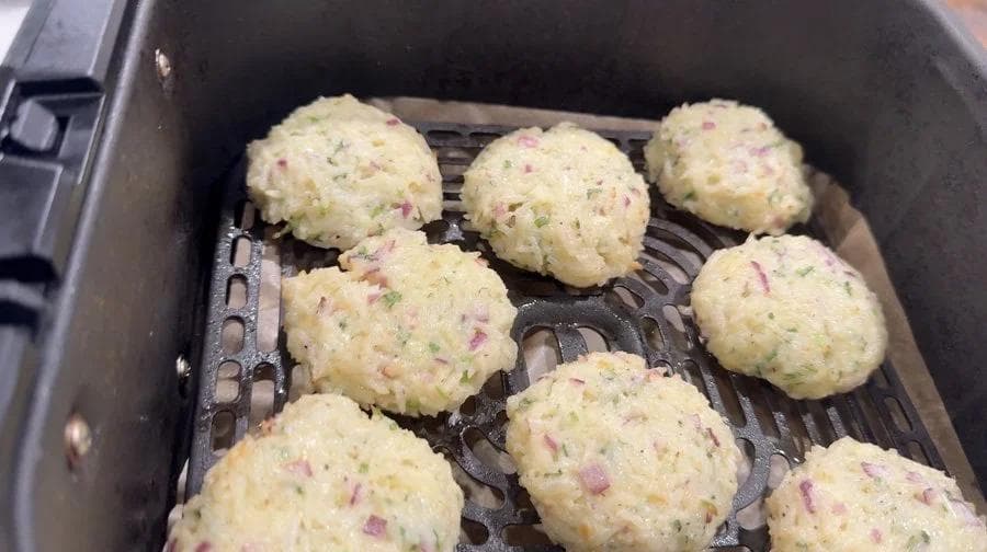 Golden-brown Venezuelan rice fritters with cheese and ham pieces arranged in an air fryer basket during cooking.