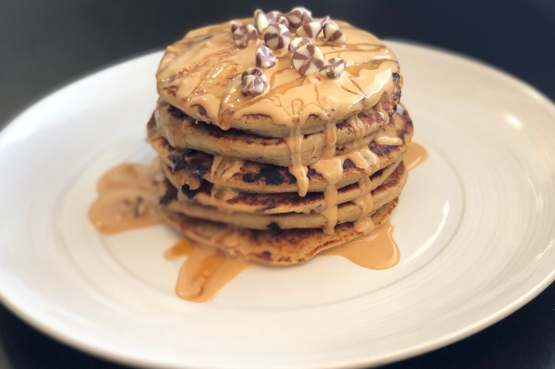 Stack of chocolate swirl pancakes topped with peanut butter drizzle and chocolate chips on a white plate.