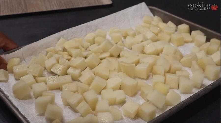Diced potatoes coated with oil spread in a single layer on a parchment-lined air fryer basket, ready to cook.