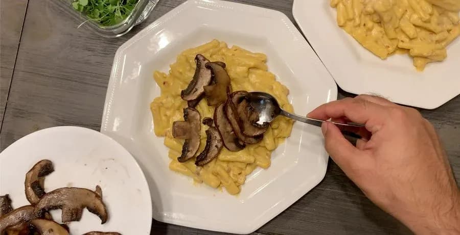 Creamy pumpkin pasta topped with sautéed mushroom slices, served on white plates with micro arugula garnish.