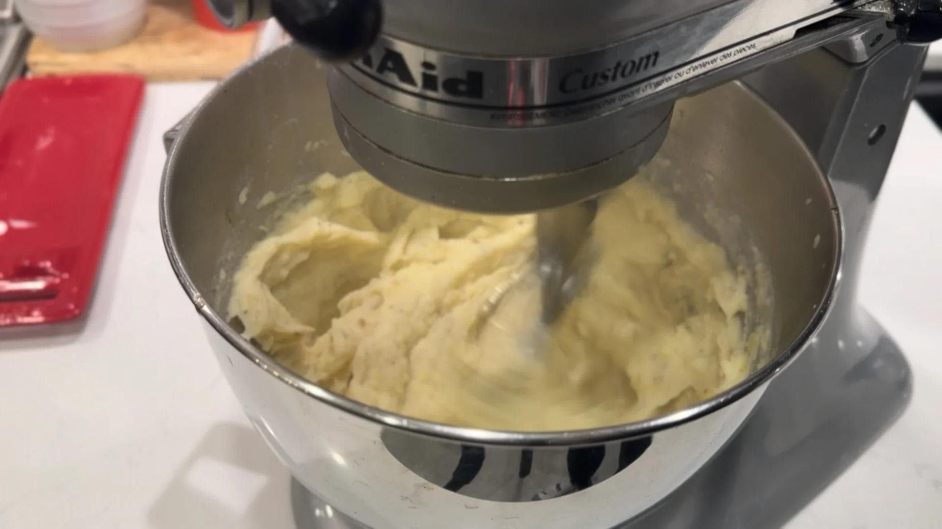 Stand mixer with paddle attachment mixing creamy garlic-herb mashed potatoes to smooth consistency.