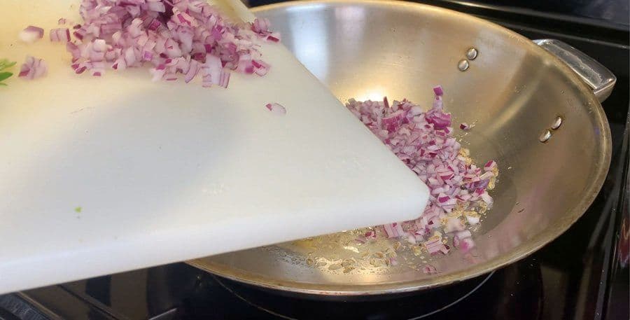 Diced red onions being sautéed in a wok with oil and butter on a stovetop.