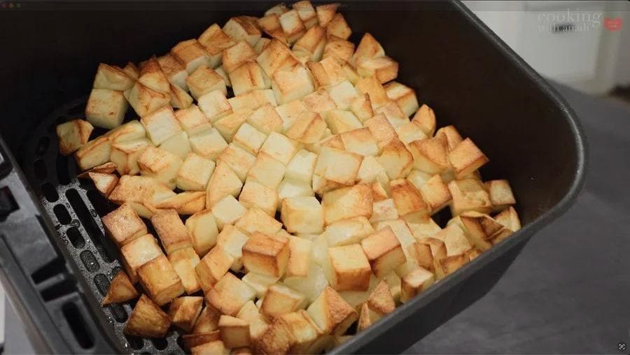 Golden-brown diced potatoes in an air fryer basket during cooking, showing even crisping and browning.