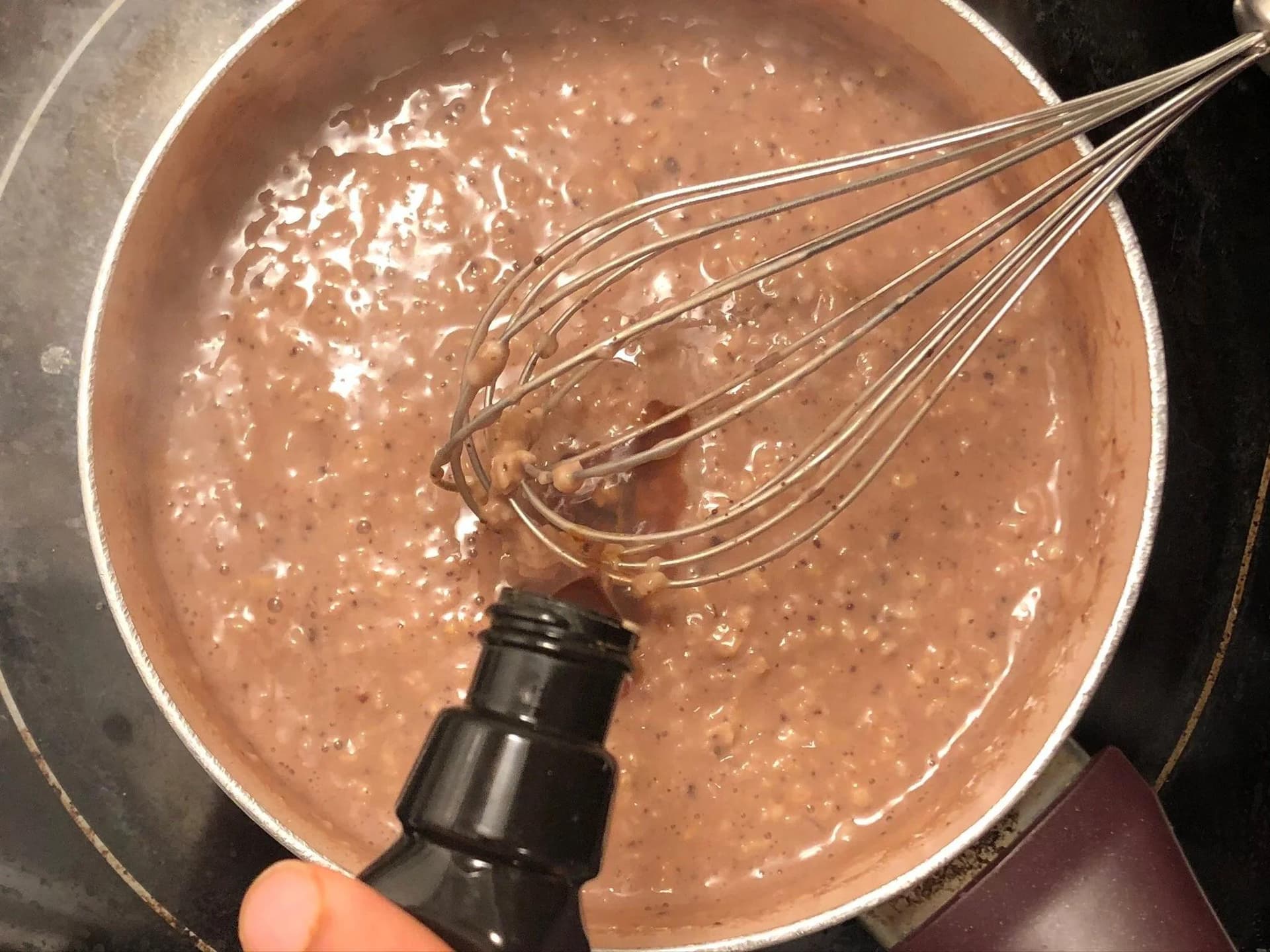 Whisking chocolate oatmeal mixture in a pot, combining cocoa powder, milk, and oats into smooth batter.