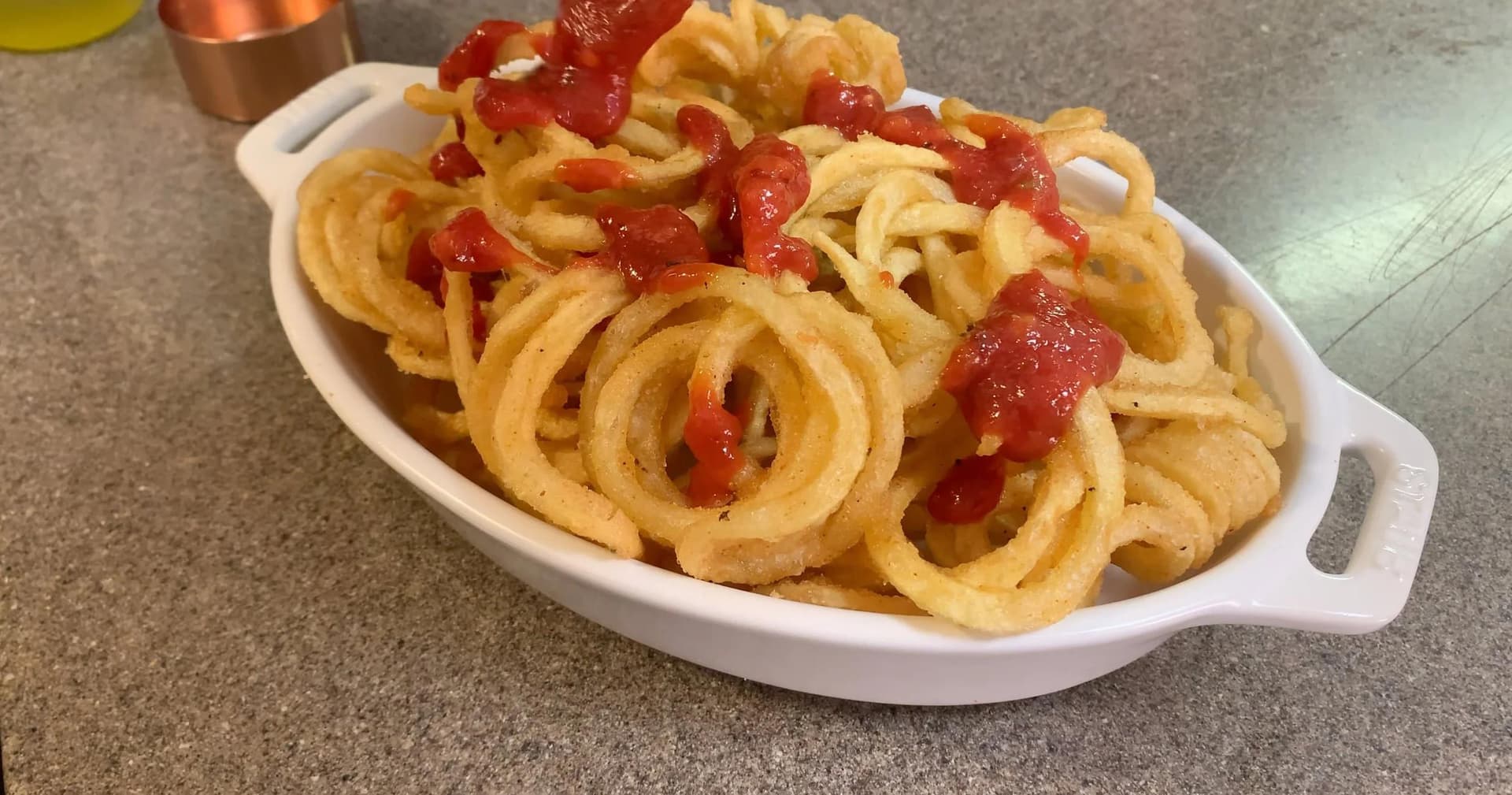 Onion rings topped with red tomato sauce in a white oval casserole dish.