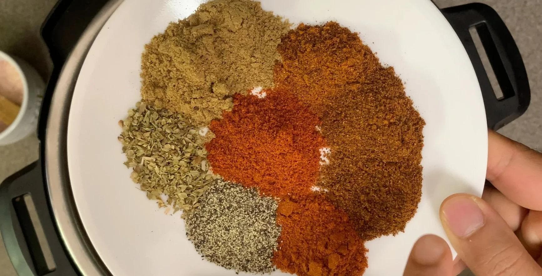 Spices measured in white bowl: cumin, chili powder, oregano, and black pepper ready to be added to chili.