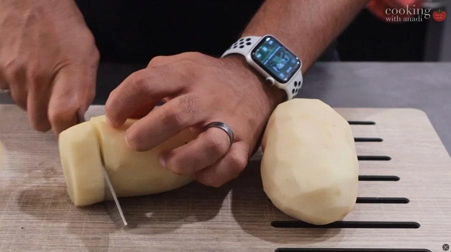 Hands cutting peeled potatoes into cubes on a cutting board with measurement lines.