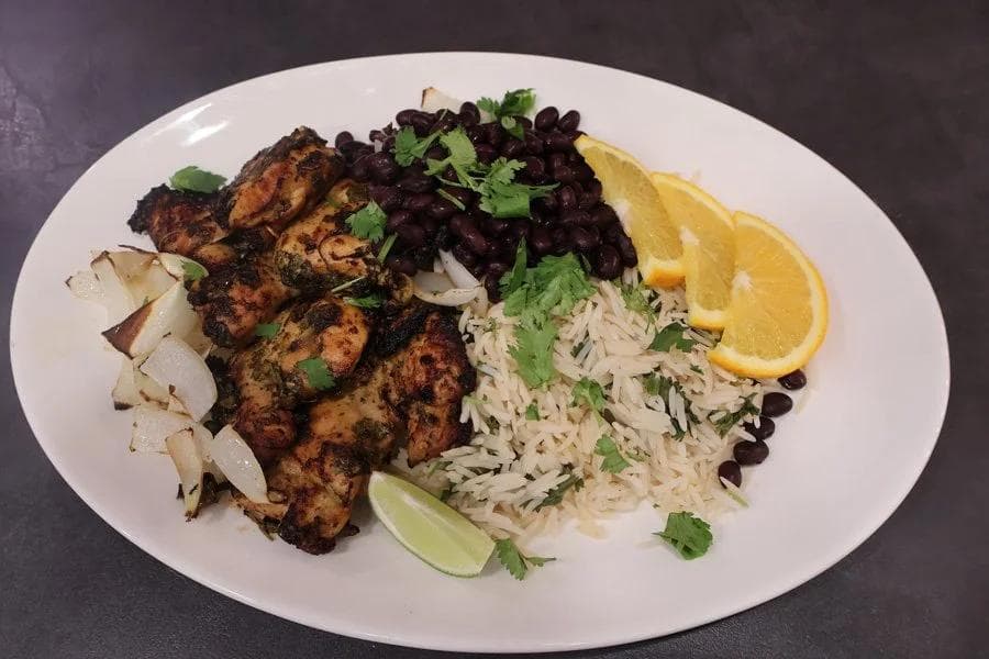 Plated Cuban mojo chicken with rice, black beans, grilled onions, cilantro, and lime wedge garnish.