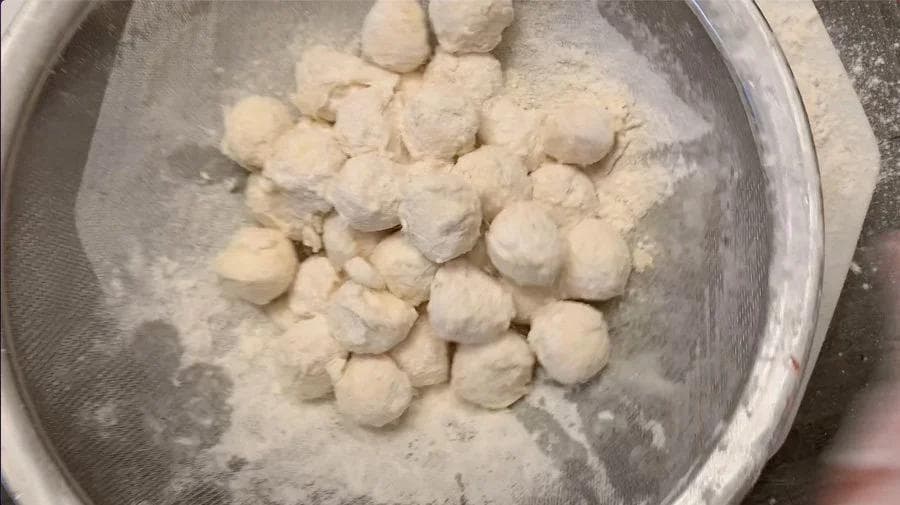 Breaded mozzarella balls coated in breadcrumbs in a white colander, ready to be frozen.