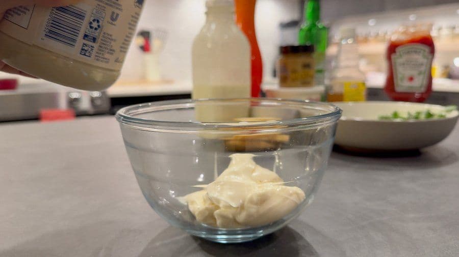 Mayonnaise being poured into a glass bowl containing ranch dip ingredients during preparation.