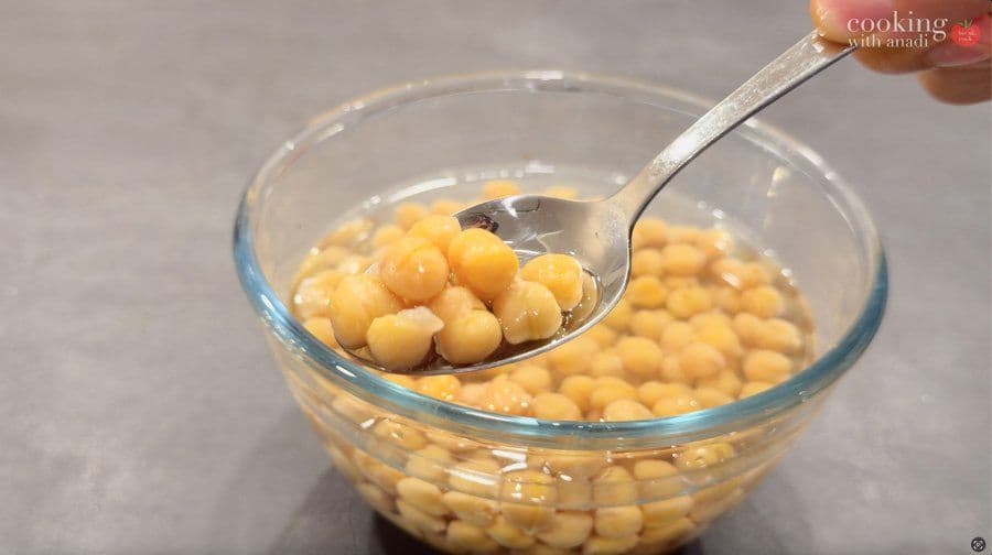 Cooked chickpeas being lifted with a spoon from a bowl of liquid, showing moisture content.