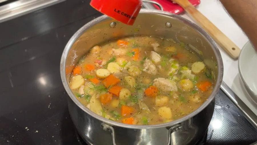 Pot of simmering country harvest chicken stew with potatoes, carrots, celery, and herbs in broth.