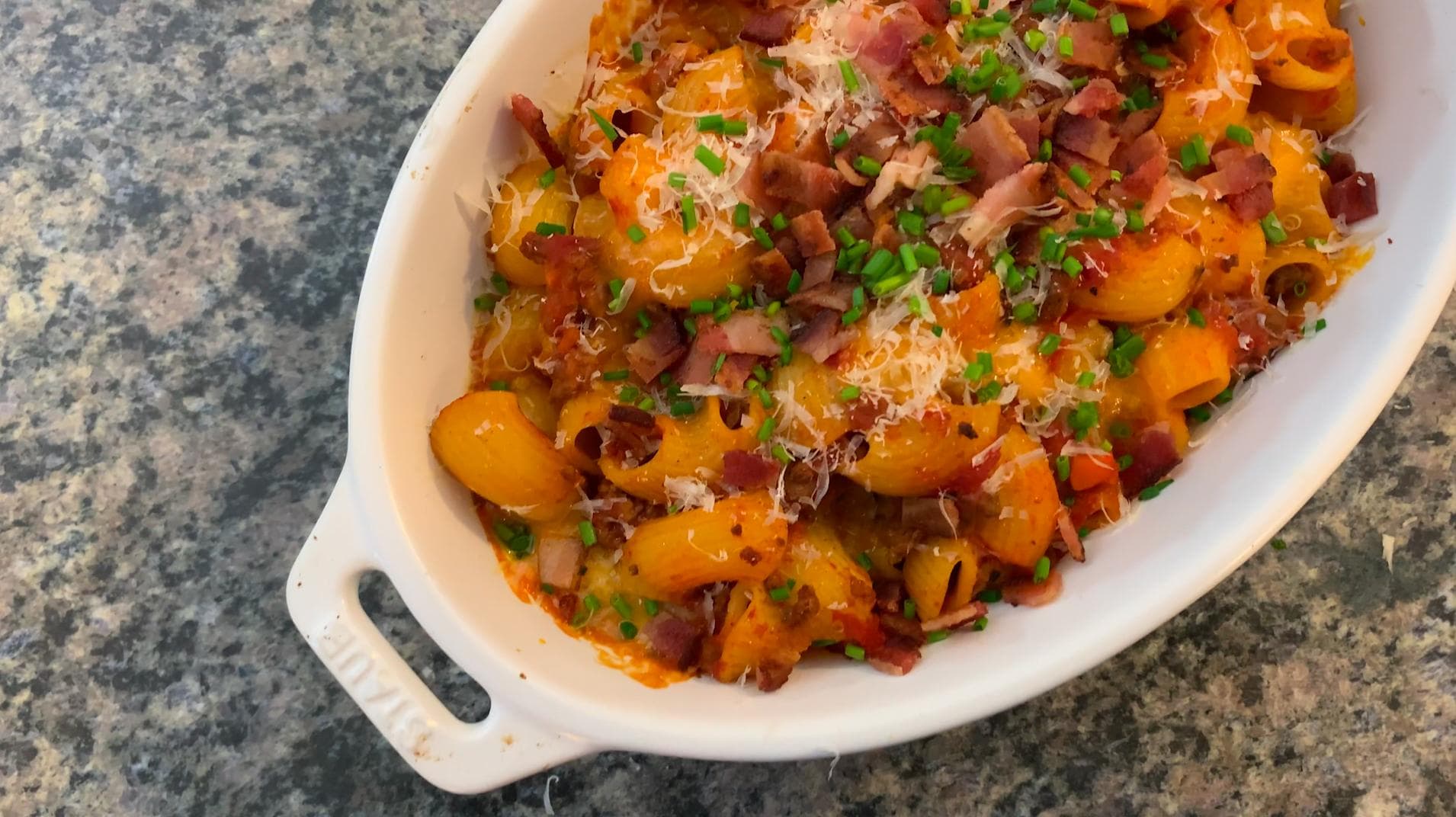 Baked mac and cheese topped with crispy bacon, melted cheese, and fresh green onions in a white baking dish.