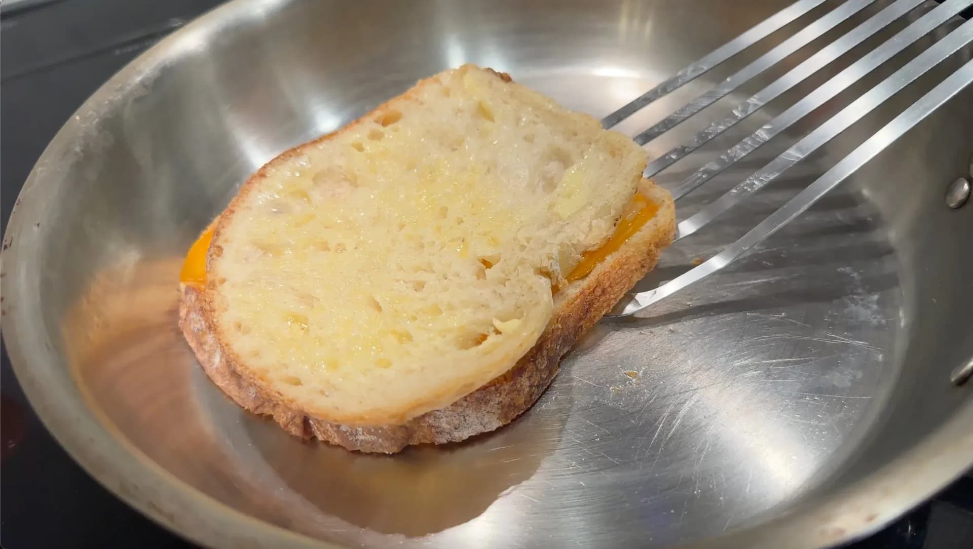 Golden-brown grilled cheese sandwich in a stainless steel pan with melted cheese visible inside.