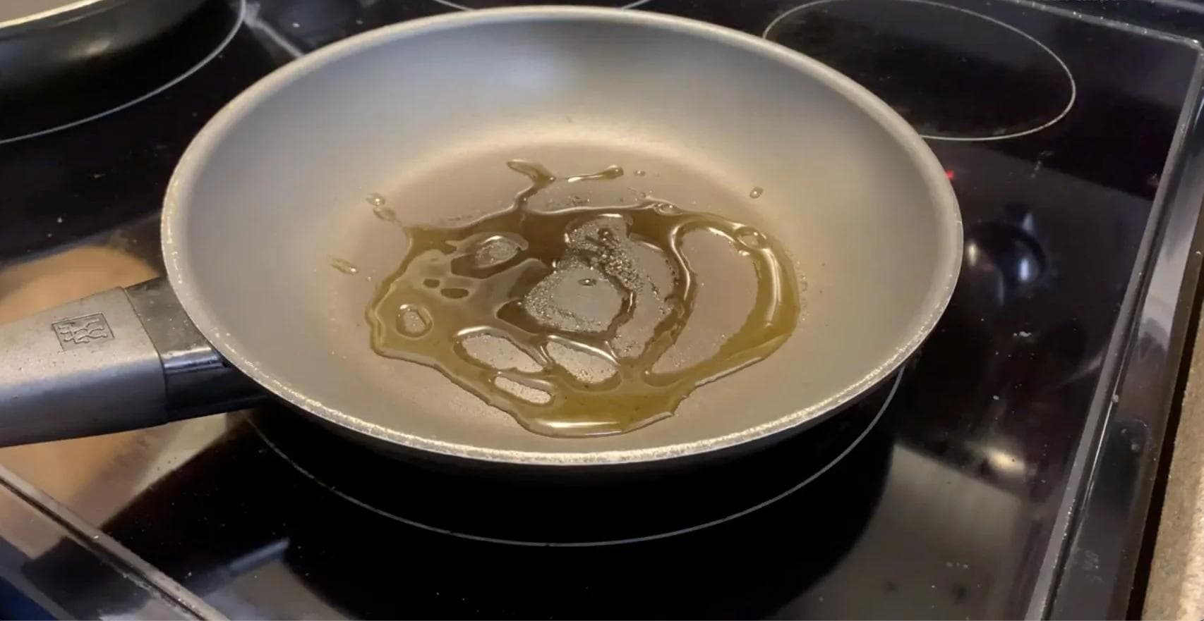 Diced squash and eggplant searing in olive oil in a white ceramic pan on a stovetop.