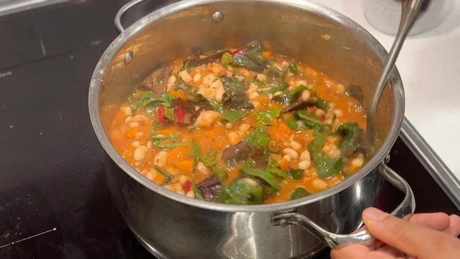 White bean harissa stew simmering in a pot with rainbow chard, chickpeas, and fresh herbs.