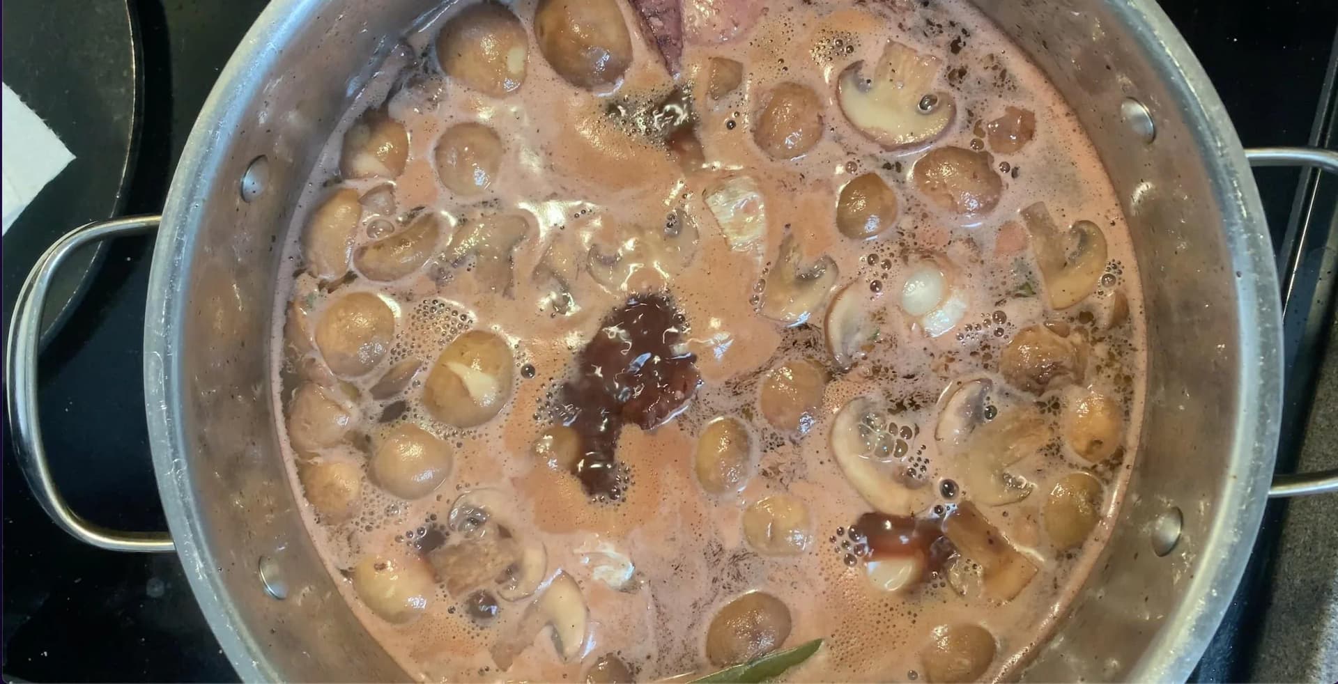 Coq au vin simmering in a pot with mushrooms, bacon, and chicken in a rich brown wine sauce.