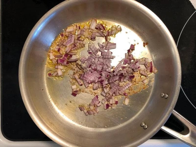 Diced red onions sautéing in bacon and chorizo fat in a stainless steel pan