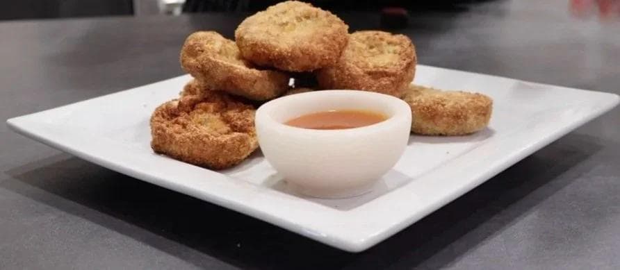 Golden crispy air fryer chicken nuggets arranged on a white plate with a small bowl of dipping sauce in the center.