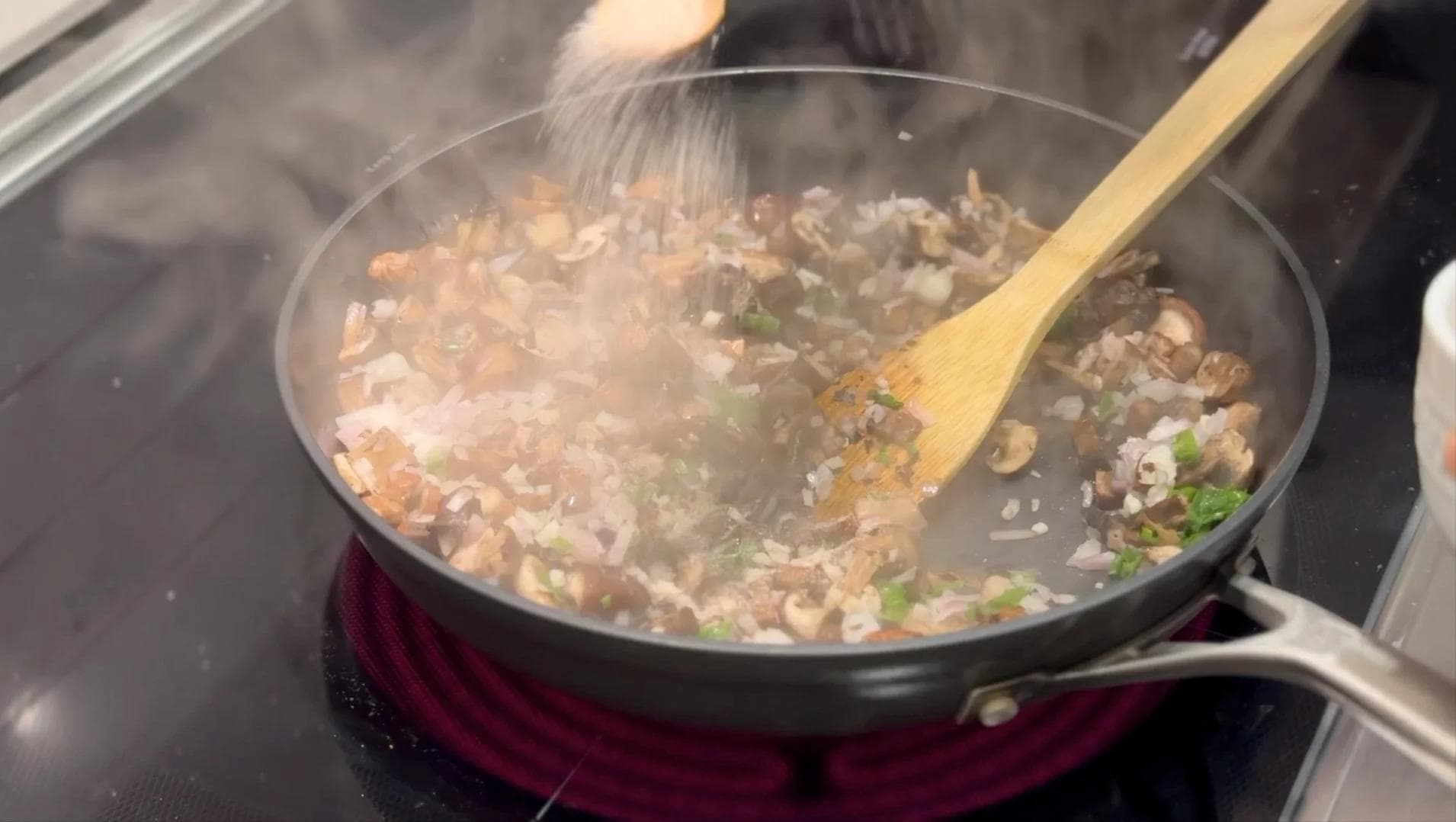 Sautéed mushrooms with shallots and garlic cooking in a pan, being stirred with a wooden spoon.