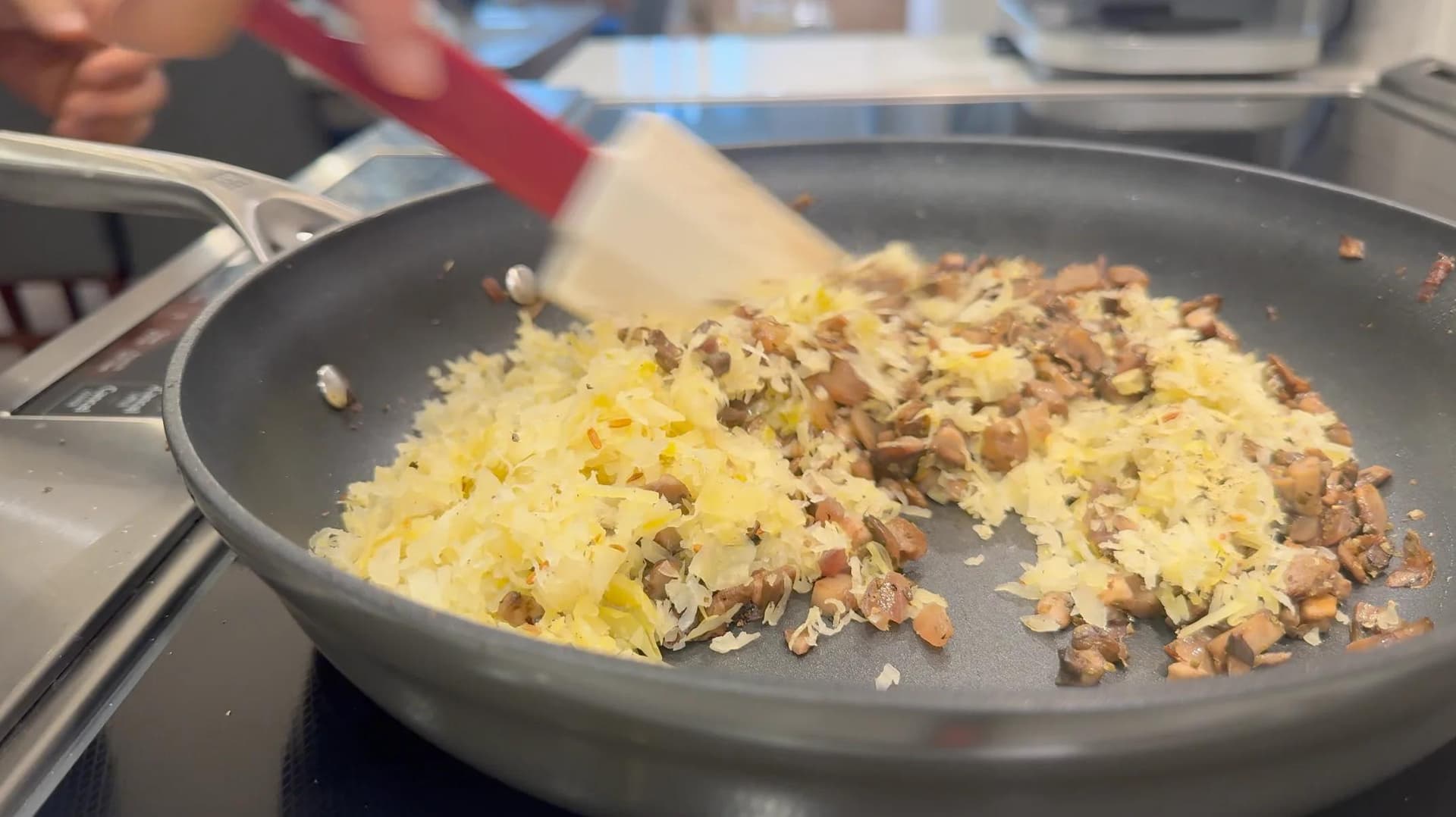 Sauerkraut and ground meat mixture cooking in a gray skillet on stovetop, being stirred with a spatula.