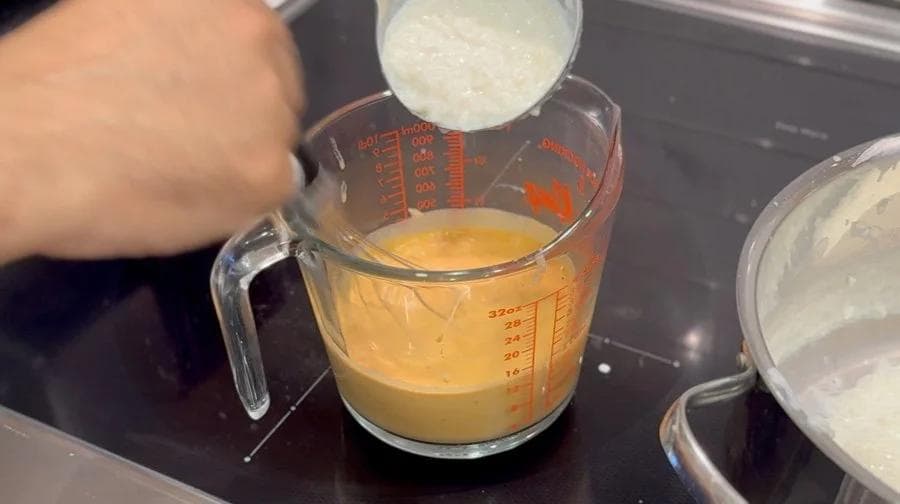 Tempering egg mixture being poured into measuring cup of pumpkin rice pudding base.