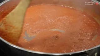 Tomato-based masala sauce simmering in a pan with a wooden spoon, showing oil separation and a rich reddish-brown color.