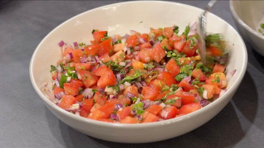 Freshly made pico de gallo in a white bowl, combining diced tomatoes, red onions, cilantro, and lime juice.