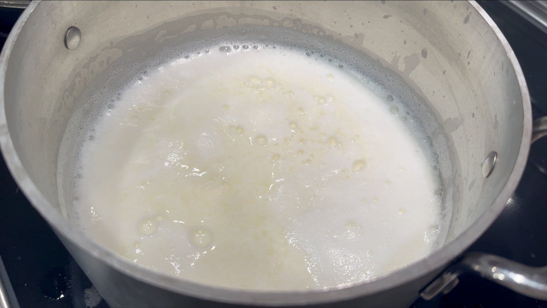Milk curdling in a pot with visible curds separating from whey during homemade ricotta cheese making.