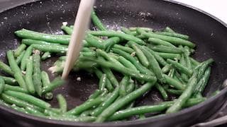 Sautéed green beans with garlic and coconut flakes being stirred in a non-stick pan during cooking.