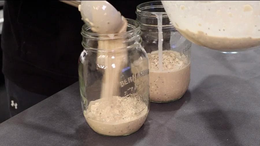 Oat mixture being spooned into mason jars for overnight oats preparation.