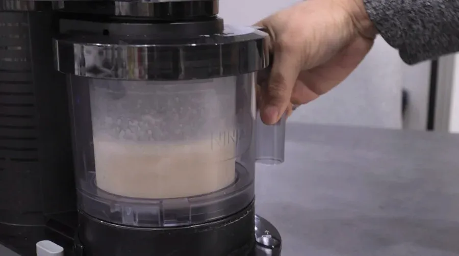 Hand holding a clear container of creamy white mixture in a Ninja Creami machine after processing.