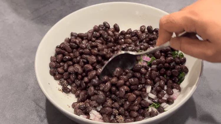 Black beans mixed with diced onions, cilantro, and lime juice in a white bowl with a fork.
