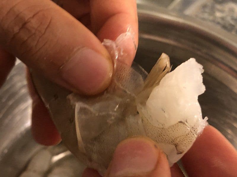 Hands demonstrating how to remove shrimp tail by pinching and pulling the shell away from the meat.