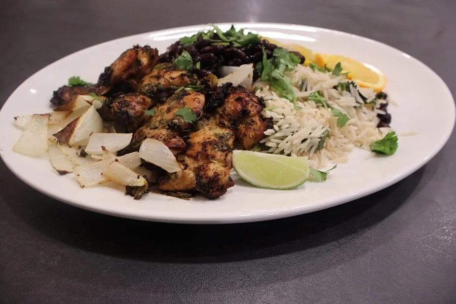 Cuban mojo chicken with caramelized onions, cilantro rice, and lime wedge on white plate.