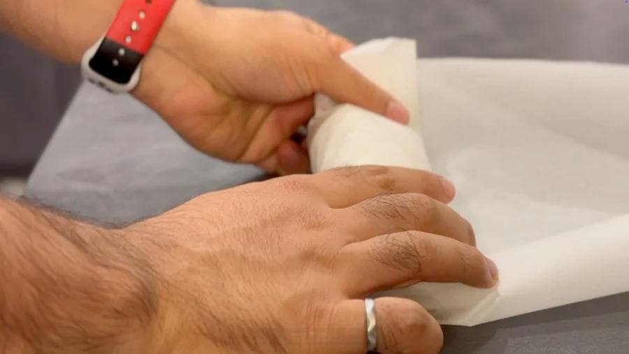 Hands wrapping a breakfast burrito in parchment paper for freezer storage.