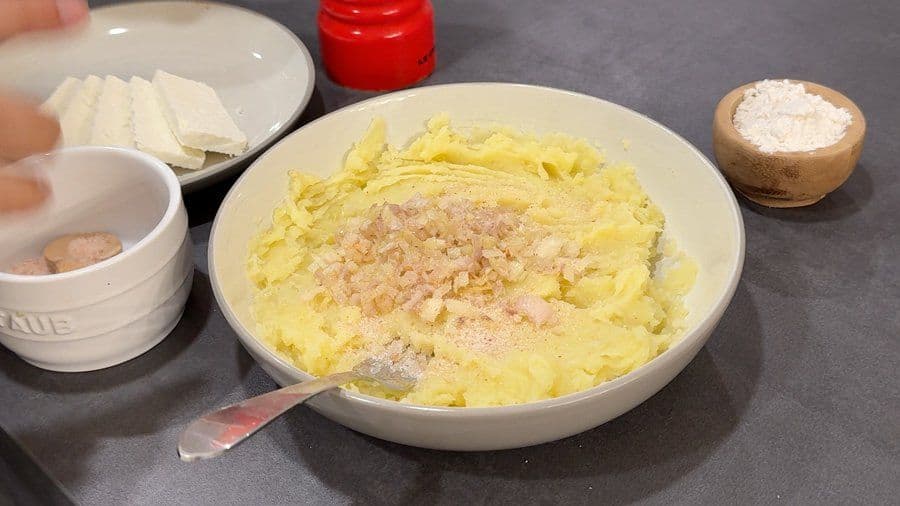Mashed potatoes with sautéed shallots in a white bowl, ready to be formed into llapingachos.