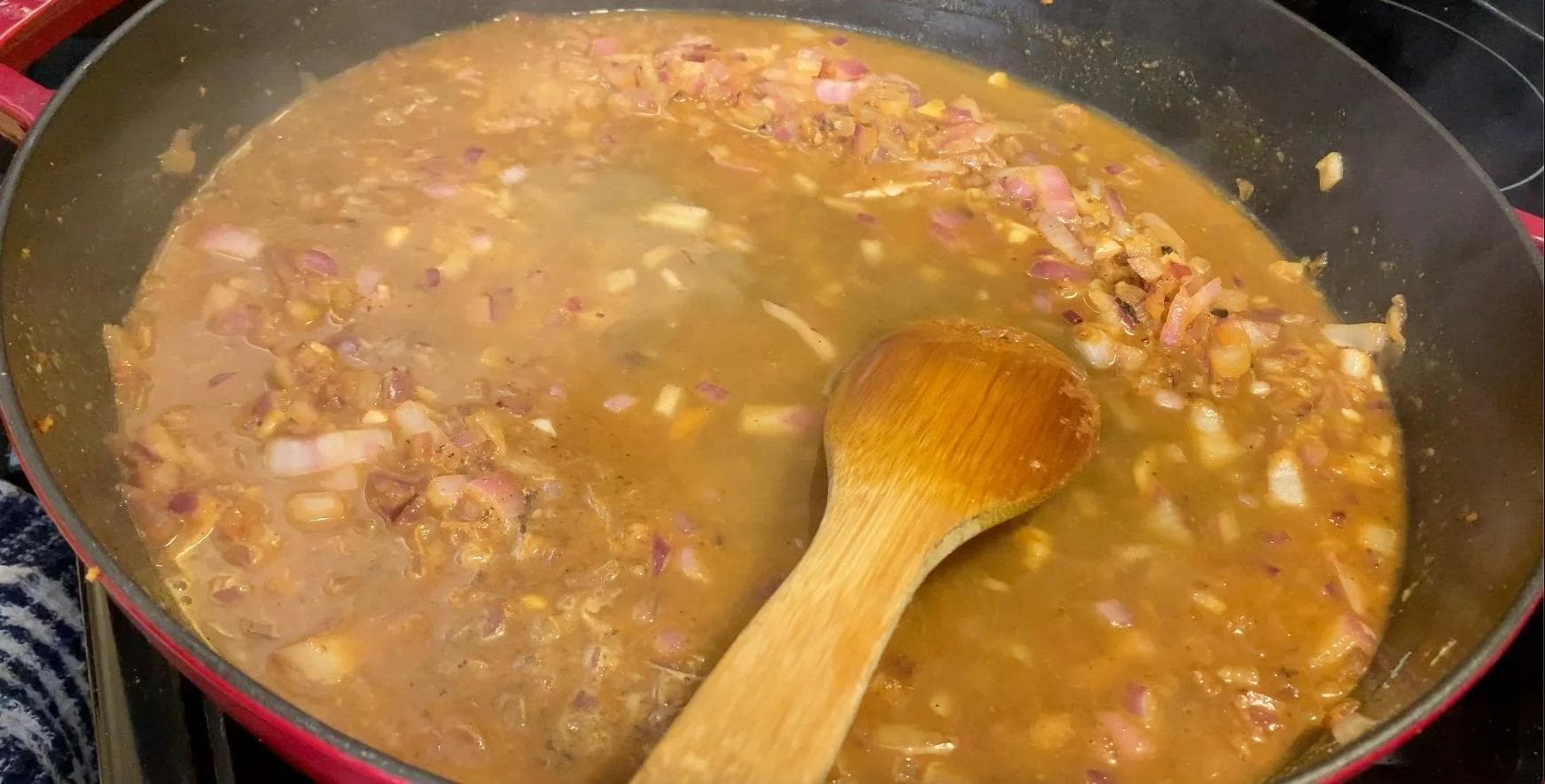 One-pot Moroccan stew with browned meat, onions, and golden broth being stirred with a wooden spoon.