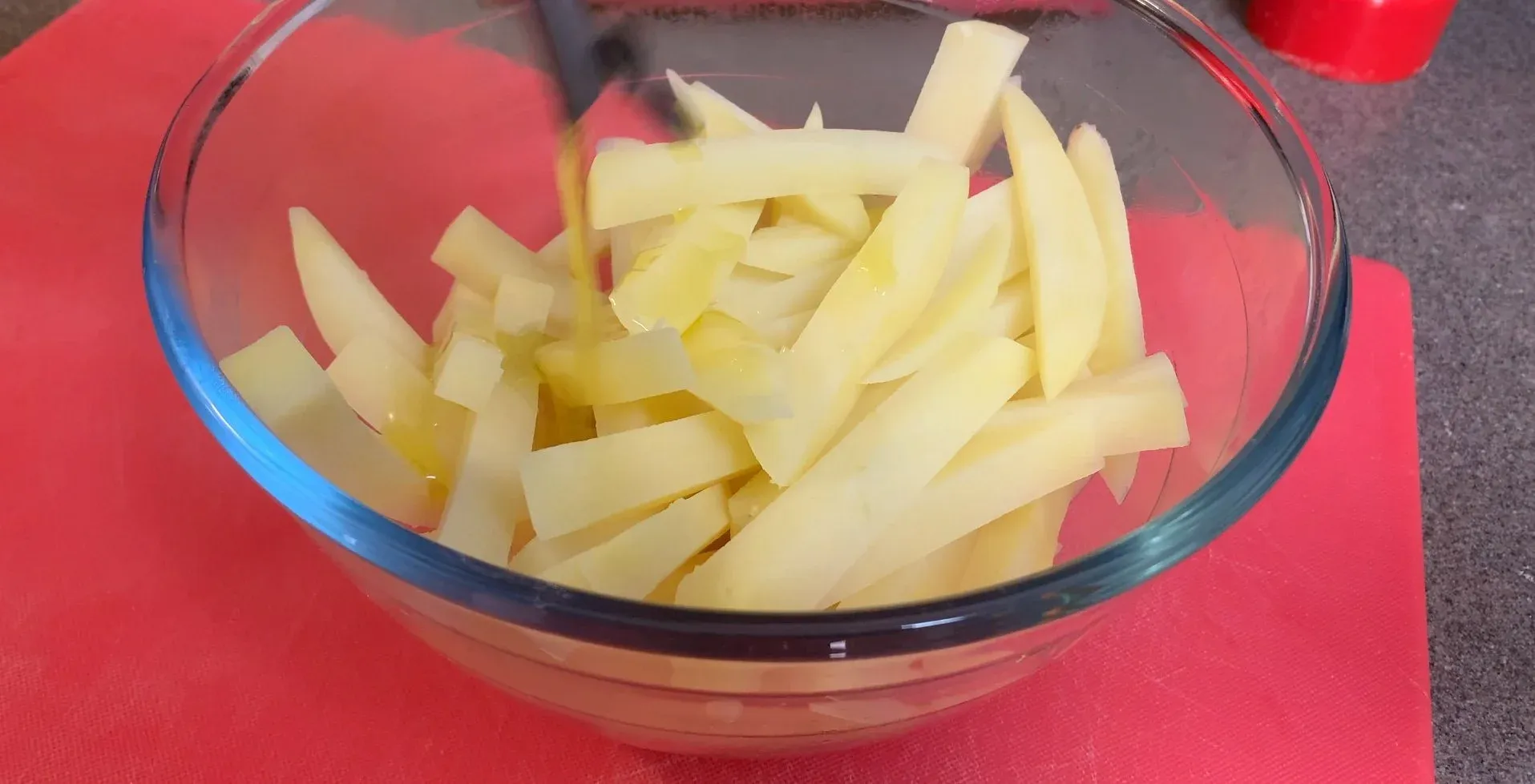 Partially cooked potato fries in a glass bowl, drained and ready to be coated with olive oil.