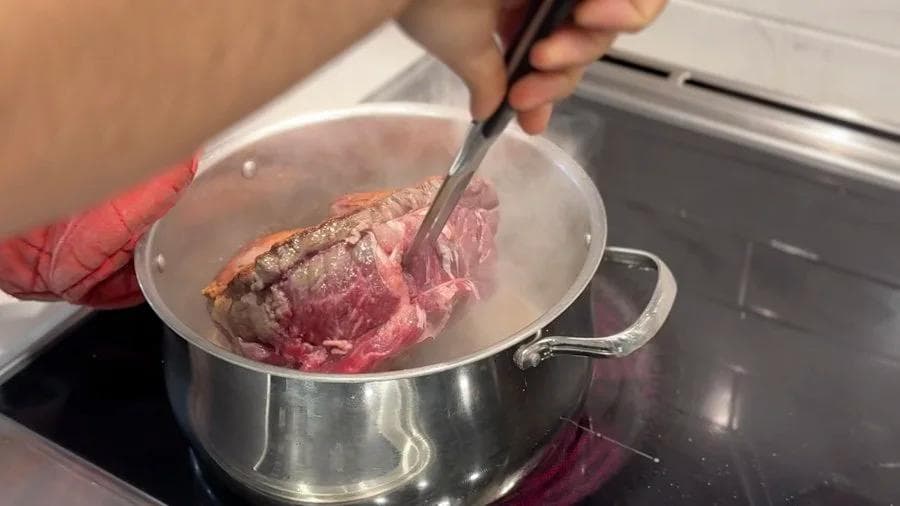 Searing a beef pot roast in a stainless steel pot, showing the browned meat being turned with tongs.