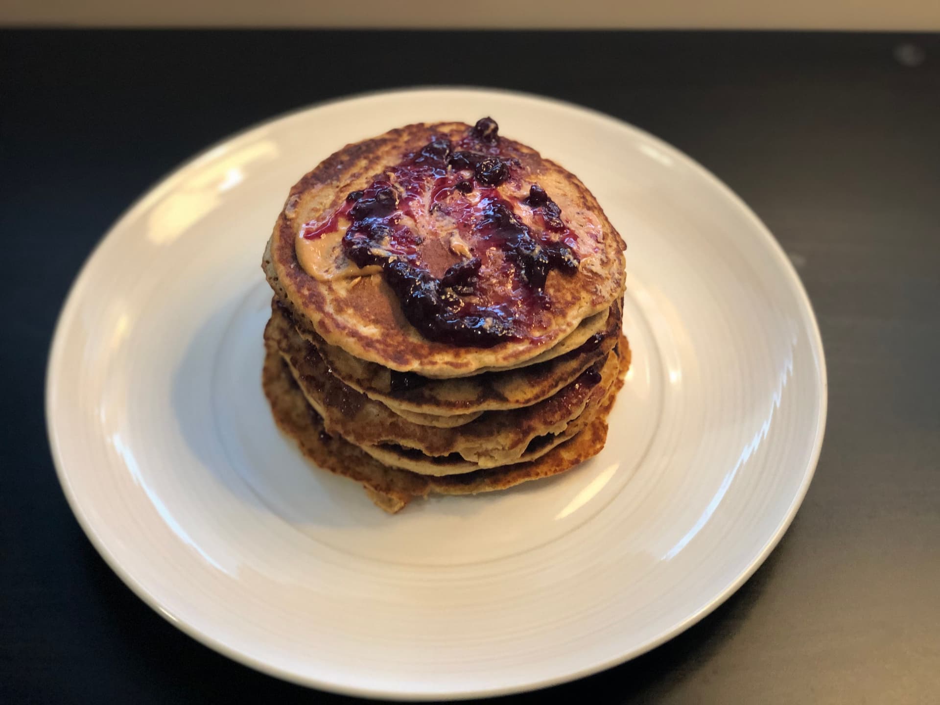 Stack of three peanut butter jelly pancakes topped with berry compote on a white plate.