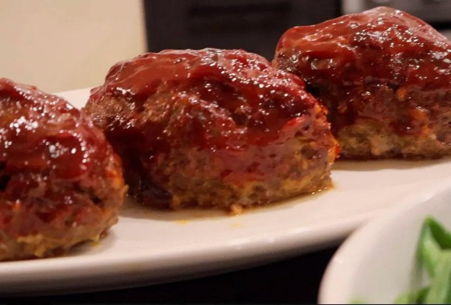 Four glazed chipotle mini meatloaves with shiny red topping on a white plate, garnished with bacon bits.