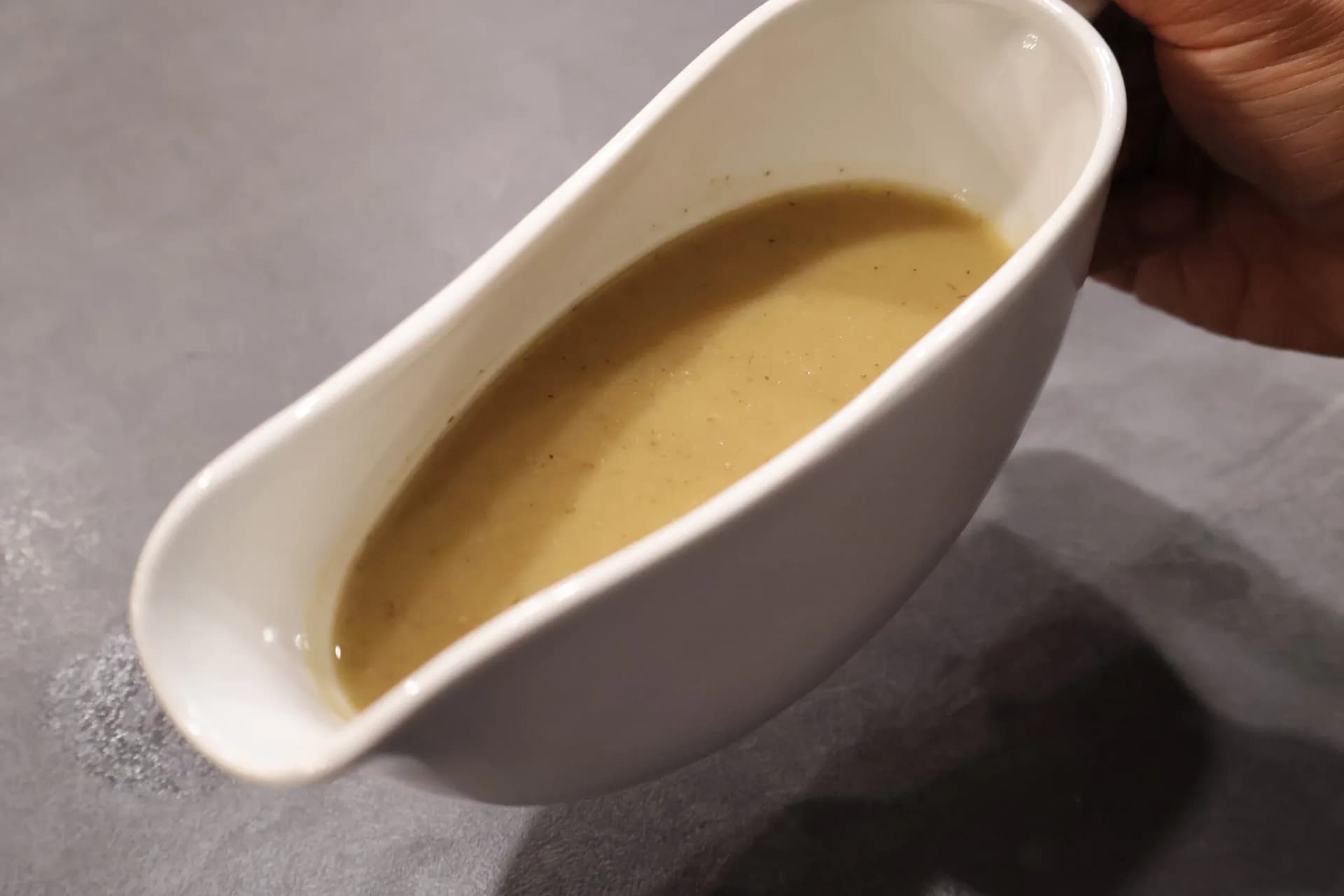 Homemade chicken gravy in a white gravy boat, tilted toward the camera to show its smooth texture