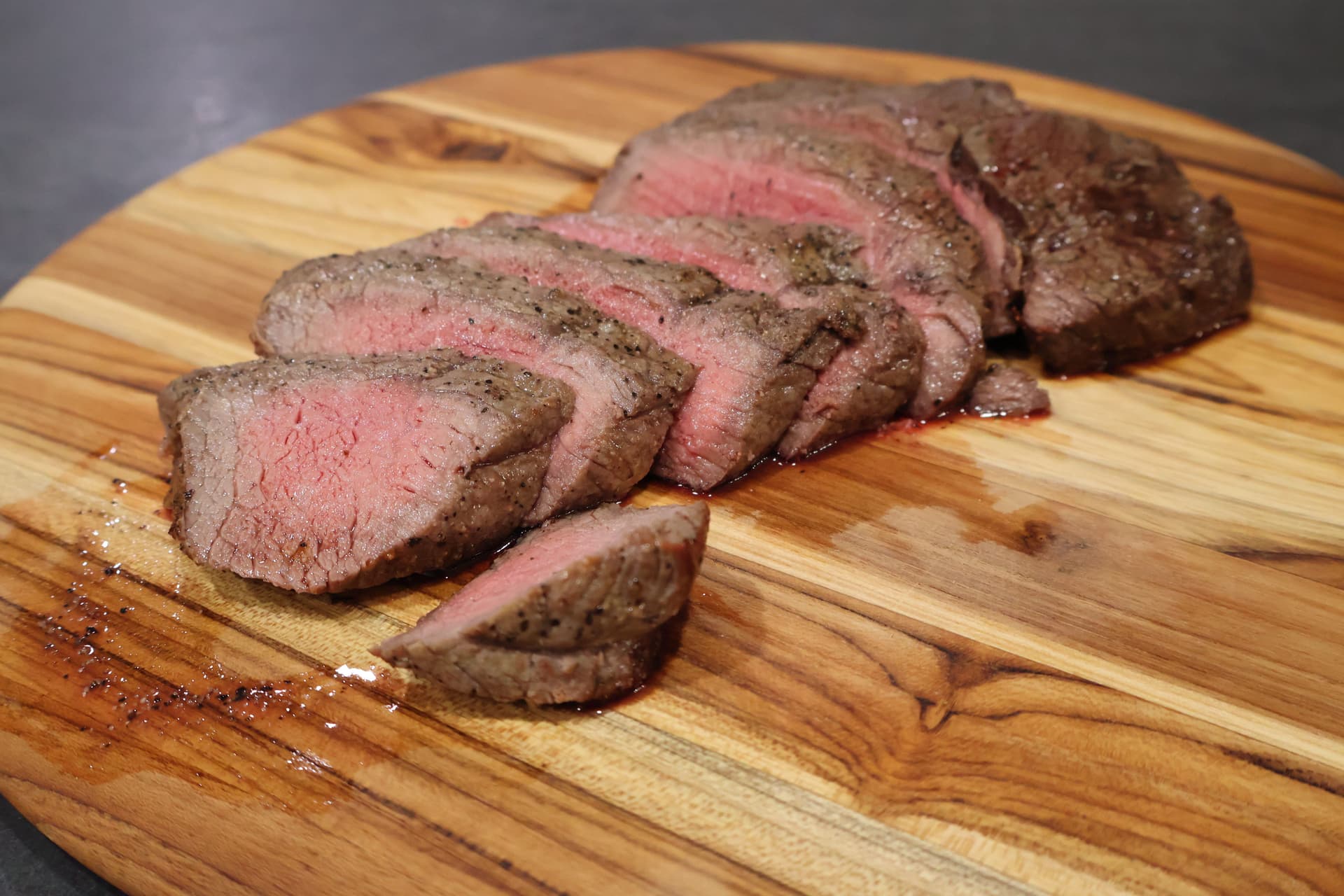 Sliced medium-rare sirloin steak with pink center on a wooden cutting board, seasoned with herbs.