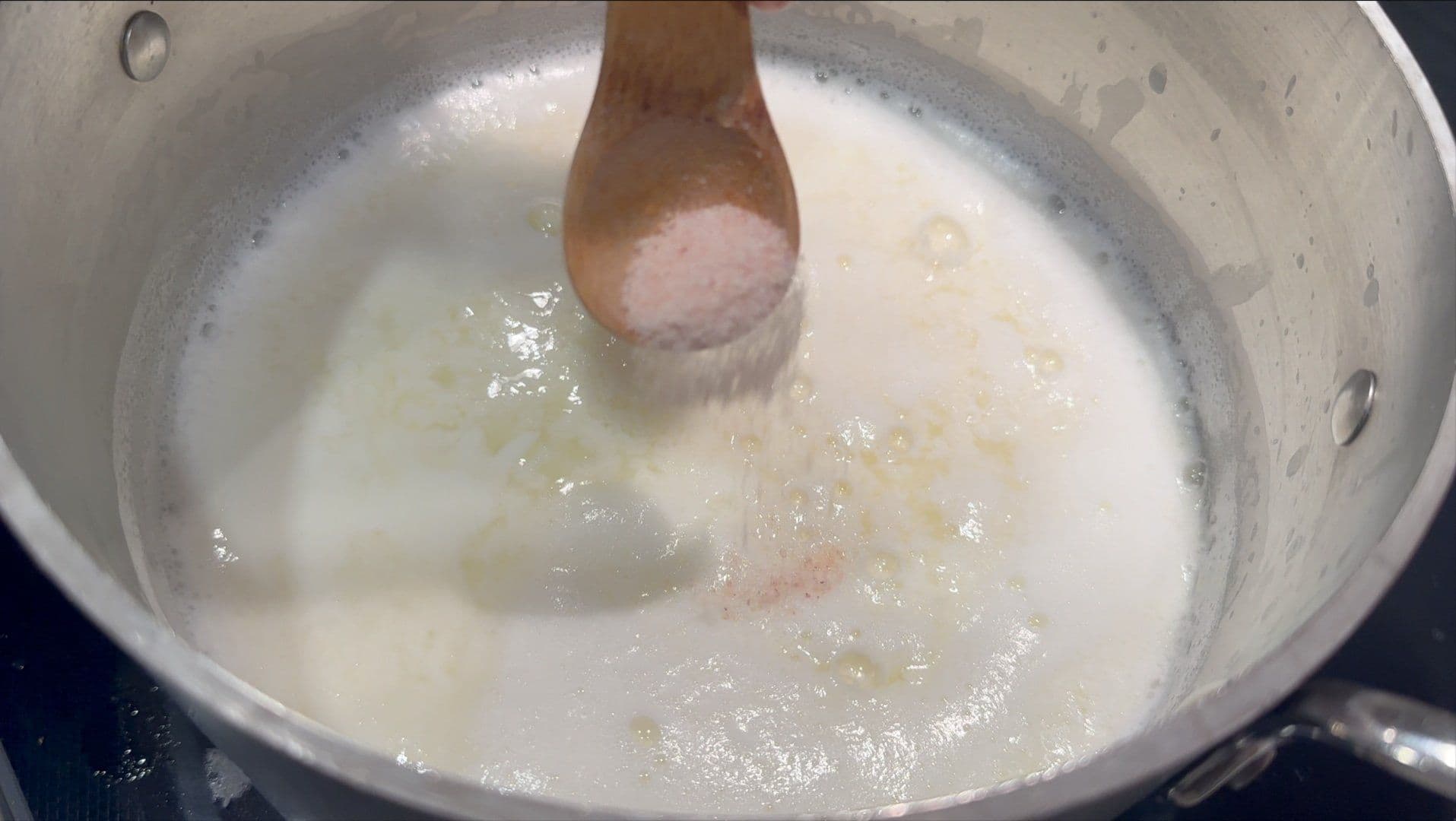 Milk curdling in a pot with a wooden spoon stirring the white curds separating from translucent whey.